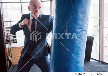 An angry bald businessman beats a boxing pear in the gym. concept of anger management An angry bald businessman beats a boxing pear in the gym. concept of anger management 122832632