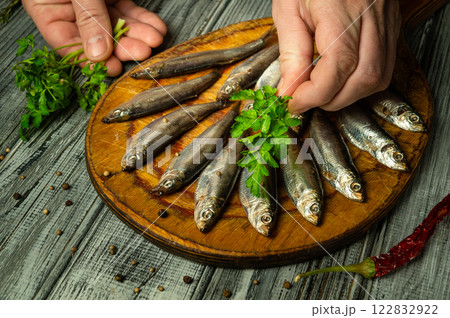 Hands delicately arrange fresh fish on a wooden platter, adding vibrant herbs or parsley. The rustic kitchen ambiance enhances the culinary artistry, inviting a feast of flavors Hands delicately arrange fresh fish on a wooden platter, adding vibrant herbs or parsley. The rustic kitchen ambiance enhances the culinary artistry, inviting a feast of flavors 122832922