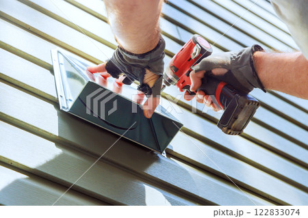 Worker is attaching ventilation cover to siding of house using power screwdriver tool Worker is attaching ventilation cover to siding of house using power screwdriver tool 122833074