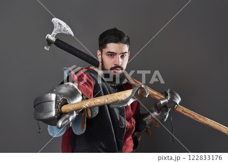 Medieval knight on grey background. Portrait of brutal dirty face warrior with chain mail armour red and black clothes and battle axe 122833176