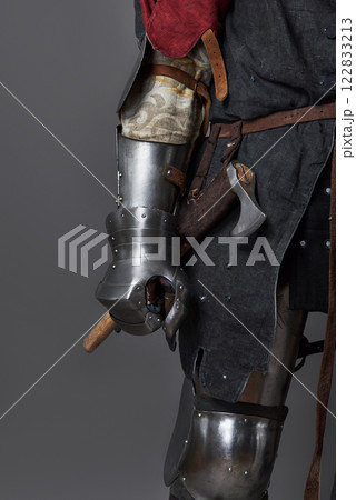 Medieval knight on grey background. Portrait of brutal dirty face warrior with chain mail armour red and black clothes and battle axe 122833213