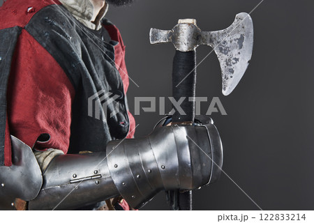 Medieval knight on grey background. Portrait of brutal dirty face warrior with chain mail armour red and black clothes and battle axe 122833214