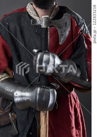 Medieval knight on grey background. Portrait of brutal dirty face warrior with chain mail armour red and black clothes and battle axe 122833216