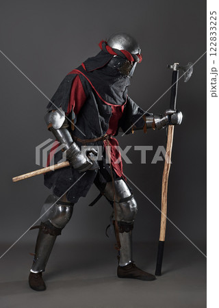 Medieval knight on grey background. Portrait of brutal dirty face warrior with chain mail armour red and black clothes and battle axe Medieval knight on grey background. Portrait of brutal dirty face warrior with chain mail armour red and black clothes and battle axe 122833225