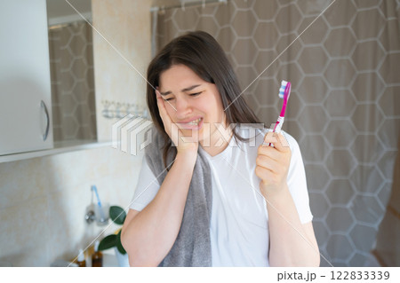Brushing with pain: Girl perseveres, continuing to care for her health. She holds her cheek due to toothache but maintains her hygiene routine. Brushing with pain: Girl perseveres, continuing to care for her health. She holds her cheek due to toothache but maintains her hygiene routine. 122833339