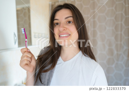 Happy woman holds a toothbrush and smiles, showing her bright smile. Regular brushing prevents tartar buildup and maintains oral health. 122833370