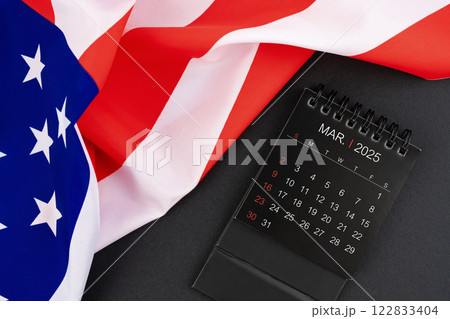 March 2025 black monthly desk calendar and United States of America flag. 122833404