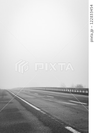 Empty highway in the fog, black and white. Bad weather on the road, monochrome. Road on foggy day in perspective with copy space. Driving conditions concept. Ghostly misty road. Caution and danger Empty highway in the fog, black and white. Bad weather on the road, monochrome. Road on foggy day in perspective with copy space. Driving conditions concept. Ghostly misty road. Caution and danger 122833454