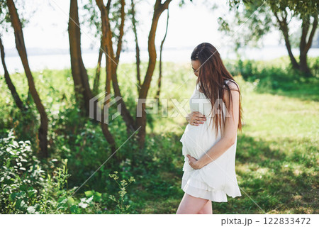 Happy pregnant woman hugging her stomach on the background of park, outdoor Happy pregnant woman hugging her stomach on the background of park, outdoor 122833472