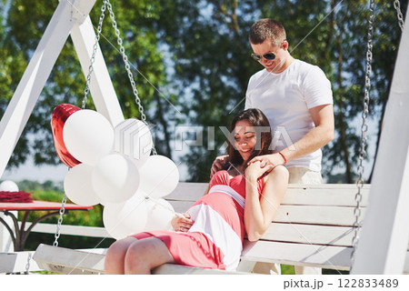 waiting baby. pregnant woman with beloved husband sit on a bench. Husband hand embraces a round belly wife. Parenthood. pregnant woman in a white dress in cherry with a red bow. close-up. nine months waiting baby. pregnant woman with beloved husband sit on a bench. Husband hand embraces a round belly wife. Parenthood. pregnant woman in a white dress in cherry with a red bow. close-up. nine months 122833489