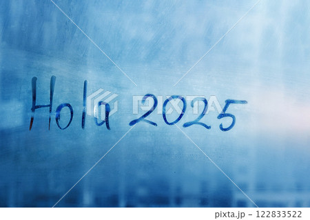 Greetings lettering Hola in Spanish is hello in english and numbers 2025 paint with finger with streaks of water on splashed by rain foggy glass on blue window Greetings lettering Hola in Spanish is hello in english and numbers 2025 paint with finger with streaks of water on splashed by rain foggy glass on blue window 122833522