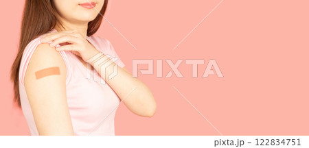 Woman showing vaccinated arm with medical adhesive bandage strip after vaccine injection over pink background. Template of HPV vaccine, world immunization day and vaccinations in pregnancy. 122834751
