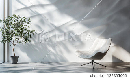 White chair is sitting in front of a wall with a plant. The chair is facing the window, and the sunlight is shining on it, creating a warm and inviting atmosphere 122835066