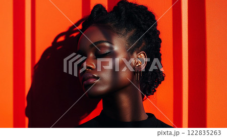 Woman with dark hair and a black shirt is standing in front of a red wall. She is looking at the camera with a calm expression Woman with dark hair and a black shirt is standing in front of a red wall. She is looking at the camera with a calm expression 122835263
