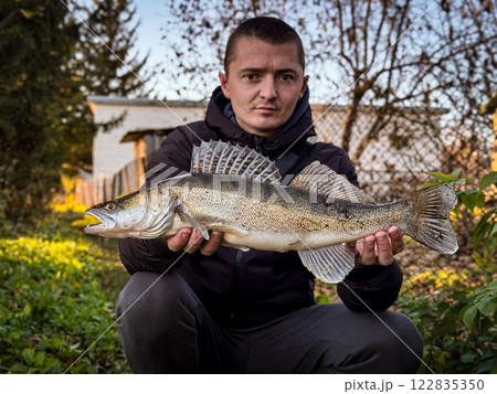 Man holds chub fish out in front of him in a boat. Portrait of smiling bearded man fishing catching fish at remote lakeside. Zander fish. Man holds chub fish out in front of him in a boat. Portrait of smiling bearded man fishing catching fish at remote lakeside. Zander fish. 122835350
