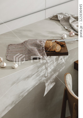 Sliced bread in linen bag on wooden board, garlic and stainless still kitchen knife. Kitchen aesthetic concept 122836445