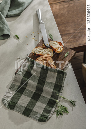Sliced bread in linen bag on wooden board, fresh herbs and stainless still kitchen knife. Kitchen aesthetic concept Sliced bread in linen bag on wooden board, fresh herbs and stainless still kitchen knife. Kitchen aesthetic concept 122836448