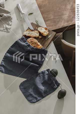 Sliced bread on wooden board, avocado, fresh herbs, linen towel and stainless still kitchen knife. Kitchen aesthetic concept 122836453
