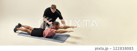 Trainer correcting man form in back extension exercise, stabilizing movement for recovery against white studio background. 122838083