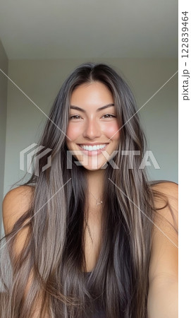 Woman with long hair smiles joyfully against a neutral background during a sunny day 122839464