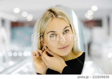 Happy woman trying on gold earrings in jewelry store Happy woman trying on gold earrings in jewelry store 122839830