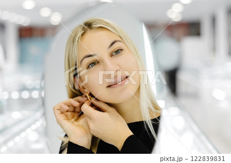 Happy woman trying on gold earrings in jewelry store Happy woman trying on gold earrings in jewelry store 122839831