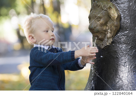 The kid washes his hands in the fountain. The boy put his fingers under the stream of water in the park The kid washes his hands in the fountain. The boy put his fingers under the stream of water in the park 122840164