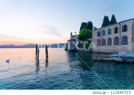 Swans on Garda Lake, Punta San Vigilio, Italy. Sunset view of historic building. Swans on Garda Lake, Punta San Vigilio, Italy. Sunset view of historic building. 122840723