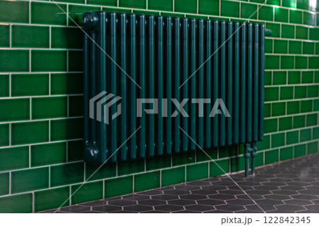 Green cast iron radiator on a tiled wall. Green tiles. 122842345
