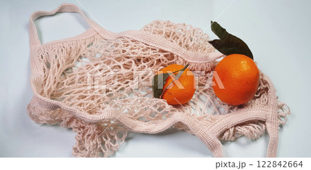 Tangerines with green leaves are placed in a white reusable food mesh bag. Nature conservation, product reuse and recycling concept, zero waste concept, eco-friendly, reasonable consumption, 122842664