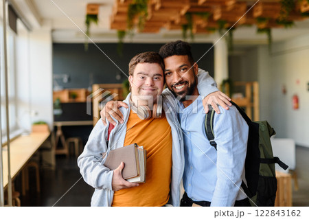 Young man with Down syndrome and his buddy with arms around looking at camera indoors at school Young man with Down syndrome and his buddy with arms around looking at camera indoors at school 122843162