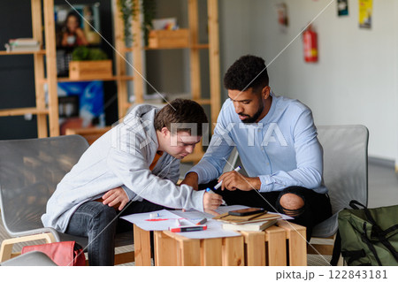 Young man with Down syndrome studyng with special educator teacher in special education classroom. 122843181
