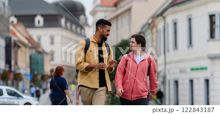 A young man with Down syndrome and his mentoring friend walking across city, talking. A young man with Down syndrome and his mentoring friend walking across city, talking. 122843187