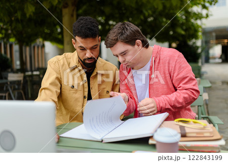 Young man with Down syndrome studyng with special educator teacher. Young man with Down syndrome studyng with special educator teacher. 122843199