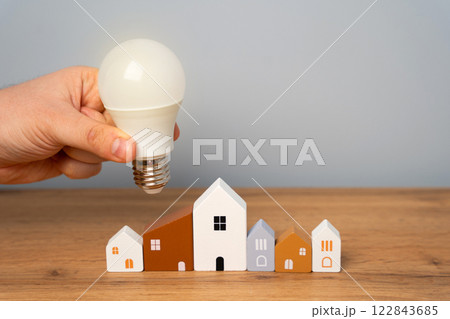 Hand holding light bulb to residential buildings. Concept of power supply. Innovations and technologies of smart home. Autonomous energy and housing. Energy saving. 122843685