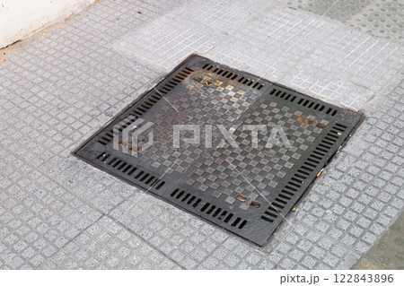 There is a manhole cover that is resting on a tiled sidewalk There is a manhole cover that is resting on a tiled sidewalk 122843896