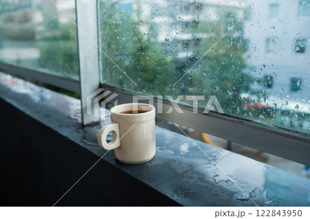 A warm cup of coffee is sitting quietly on a window sill on a rainy day outside 122843950