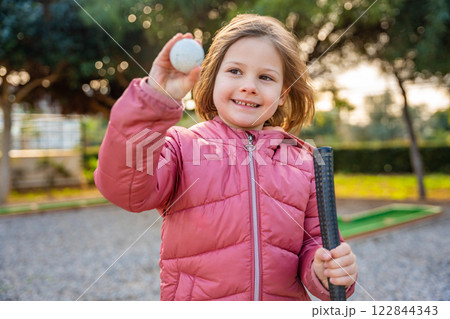 Portrait of Little girl Holding in hand Mini-Golf Ball. Little girl playing mini golf outdoor. Family vacations or resort. Portrait of Little girl Holding in hand Mini-Golf Ball. Little girl playing mini golf outdoor. Family vacations or resort. 122844343