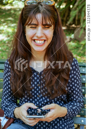 Happy young woman talking on mobile phone, sitting on bench in park 122844378