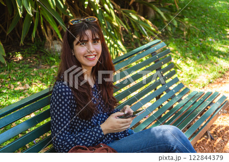 Young woman using smartphone while relaxing on park bench Young woman using smartphone while relaxing on park bench 122844379