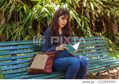 Young woman reading book while sitting on bench in park Young woman reading book while sitting on bench in park 122844381