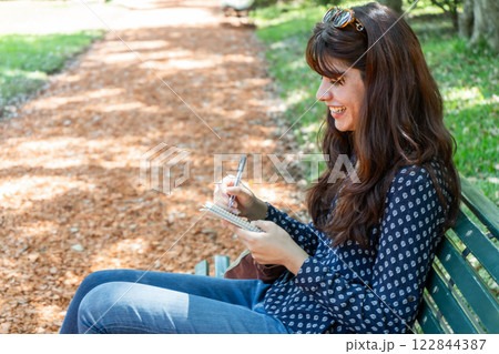 Young woman taking notes while sitting on park bench 122844387