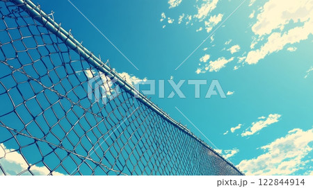 Chain link fence reaching for partly cloudy blue sky 122844914