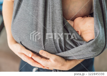 A loving mother breastfeeds her newborn baby while carrying them in a sling. A tender moment of nurturing, closeness, and maternal care, symbolizing the beauty of motherhood and the deep bond between A loving mother breastfeeds her newborn baby while carrying them in a sling. A tender moment of nurturing, closeness, and maternal care, symbolizing the beauty of motherhood and the deep bond between 122845330