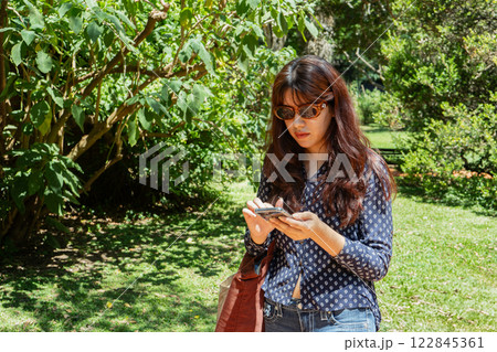 Young woman using smartphone sitting on bench in park 122845361