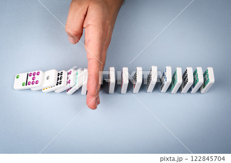 A hand stopping falling dominoes in a conceptual image of business crisis management 122845704