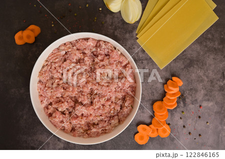 Top view raw ground minced meat in white bowl. Lasagne pasta sheets, onion, carrot, pepper. Black background. Homemade lasagna cooking preparation 122846165