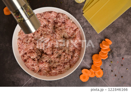 Top view raw ground minced meat in white bowl, pepper mill. Lasagne pasta sheets, carrot, pepper. Black background. Homemade lasagna cooking preparation Top view raw ground minced meat in white bowl, pepper mill. Lasagne pasta sheets, carrot, pepper. Black background. Homemade lasagna cooking preparation 122846166