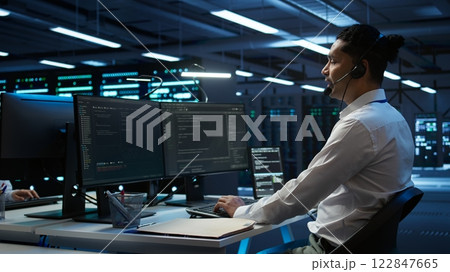 Data center computer scientist wearing mic headset, doing installation of networking equipment. Server hub IT professional talking in microphone with system administrators, camera B 122847665