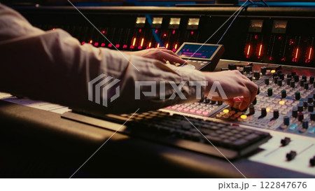 Sound designer working with sliders and switchers on control desk in professional music recording studio, editing and producing songs for a new album. Technician adjusting volume levels. Camera B. Sound designer working with sliders and switchers on control desk in professional music recording studio, editing and producing songs for a new album. Technician adjusting volume levels. Camera B. 122847676